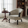 A classic upholstered armchair with a beige and gray floral pattern, dark wood arms and legs, styled in a cozy living room next to a small wooden side table and on a patterned area rug.