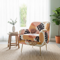 A mid-century modern armchair with a tropical leaf pattern in peach, beige, and black, styled in a bright room with a small wooden side table, a potted plant, and a woven rug.