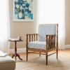 A wooden armchair with a blue and white geometric patterned cushion set, styled in a bright living room next to a small wooden side table and a framed abstract painting.