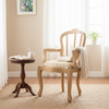 A light natural wood armchair with a cream and tan patterned upholstered seat cushion, styled in a bright room next to a small dark wood side table.