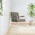 A modern minimalist interior scene featuring a gray upholstered armchair with chrome legs, several green potted plants, a white shag rug in the foreground, and a light beige area rug on a pale wood floor against a white wall.