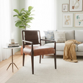 A mid-century modern accent chair with brown leather upholstery and dark wood arms and legs, positioned on a light beige patterned area rug in a bright, contemporary living room.