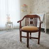 A wooden baby nursery chair with a curved back and a round tan cushion, placed on a round gray rug in a softly decorated nursery room.