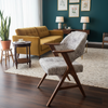 A mid-century modern accent chair with a textured gray and white woven seat and back, supported by dark wood legs, positioned in a styled living room with a mustard yellow sofa, dark teal wall, and wood flooring.
