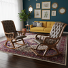 A styled living room featuring two wooden rocking chairs with tufted brown upholstery, placed on a large patterned area rug in front of a yellow sofa and a dark teal wall with framed botanical prints.