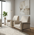 Two modern cream-colored armchairs with black metal legs, arranged on a textured light gray rug in a bright, contemporary living room with light wood floors and a large abstract painting on the wall.