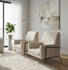 Two modern cream-colored armchairs with black metal legs, arranged on a textured light gray rug in a bright, contemporary living room with light wood floors and a large abstract painting on the wall.