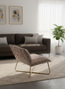 A modern living room scene featuring a brown fabric sofa, a patterned armchair with gold metal legs, a beige geometric area rug, and a potted green plant in a bright room with sheer white curtains.