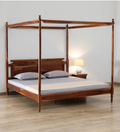 A dark brown wooden four-poster bed with a matching headboard, styled with white bedding and gray pillows, set in a bedroom with a bedside table and lamp.